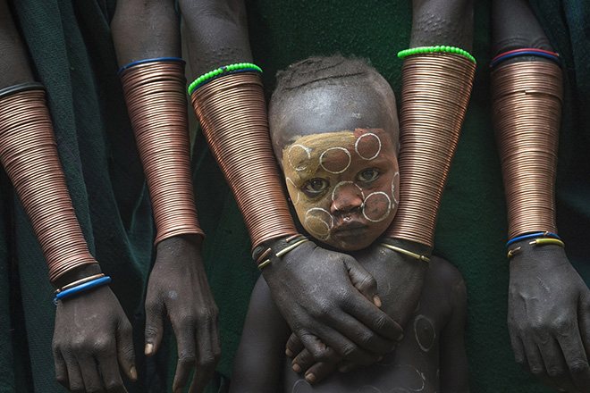 Kibish, Ethiopia. Danny Yen Sin Wong, Malaysia. Winner Best Single image in a Portfolio Faces, People, Cultures, Travel Photographer of the Year 2018. (A boy stands among the copper bracelets worn by the Suri women). (Photo: Danny Yen Sin Wong/www.tpoty.com)