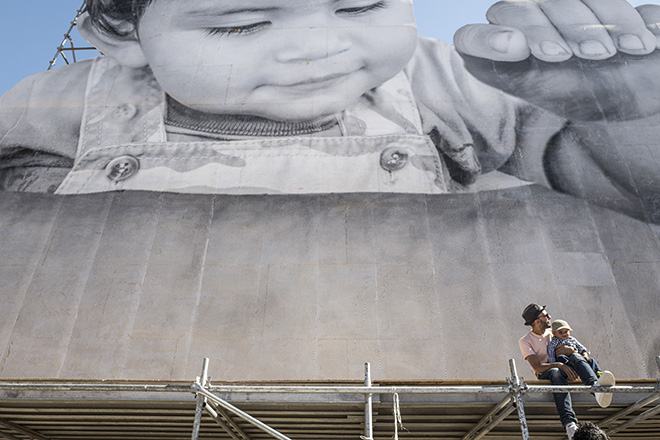 JR and Kikito on scaffolding, Tecate, Border Mexico - U.S.A., 2017, photo credit: Prune Nourry