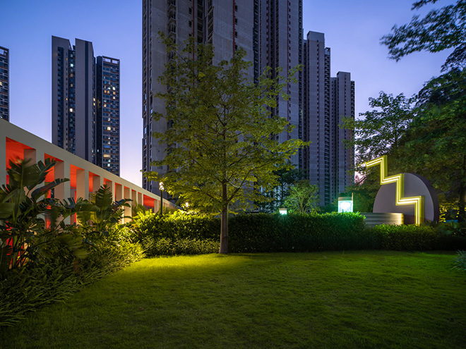 Ballistic Architecture Machine (BAM) - Buji Residences. At dusk, the yellow zigzag light activates the purple-moon dance plaza with two green landscape discoball lights, mirrored by the deep pink interior glow of the colonnade and slender high-rise towers beyond. Photo credit: Wu Qingshan