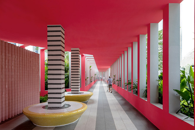 Ballistic Architecture Machine (BAM) - Buji Residences. Bold pink interior of landscape colonnade at Buji Residences, with black‑and‑white striped columns on yellow mosaic benches, surrounded by lush planting. Photo credit: Wu Qingshan