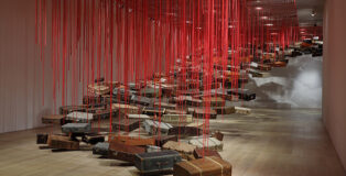 Shiota Chiharu, Accumulation - Searching for the Destination 2014/2019. Suitcase, motor and red rope. Dimensions variable. Installation view: Shiota Chiharu: The Soul Trembles, Mori Art Museum, Tokyo, 2019 Photo: Kioku Keizo. Photo courtesy: Mori Art Museum, Tokyo